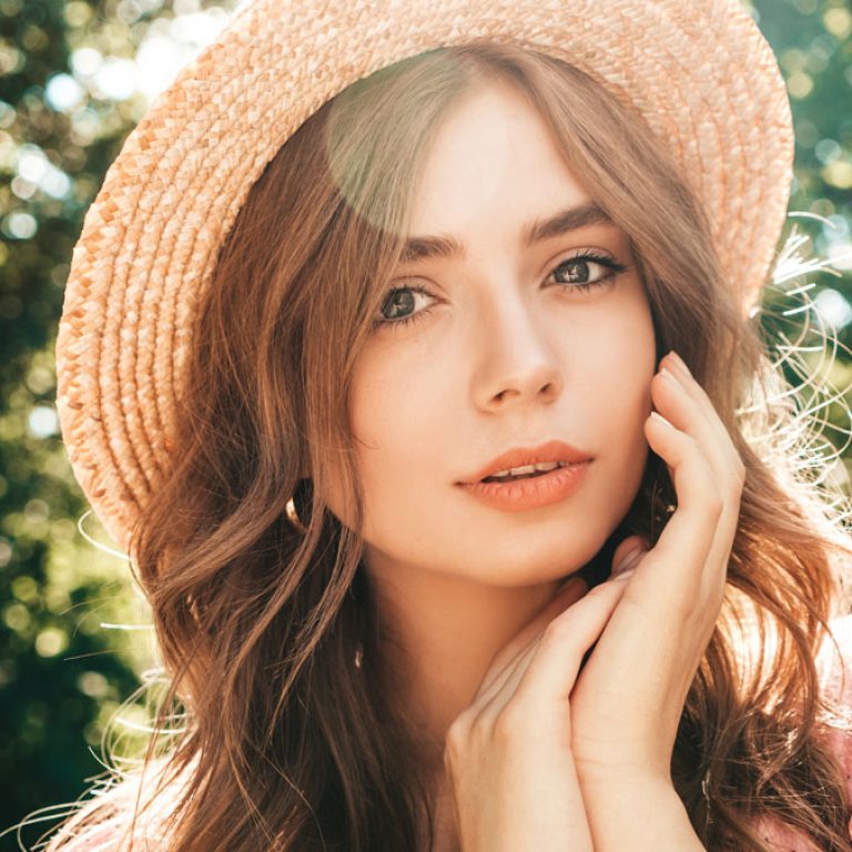 Portrait of young beautiful hipster girl in trendy summer sundress. Sexy carefree woman posing on the street background in the park in hat at sunset. Positive model outdoors